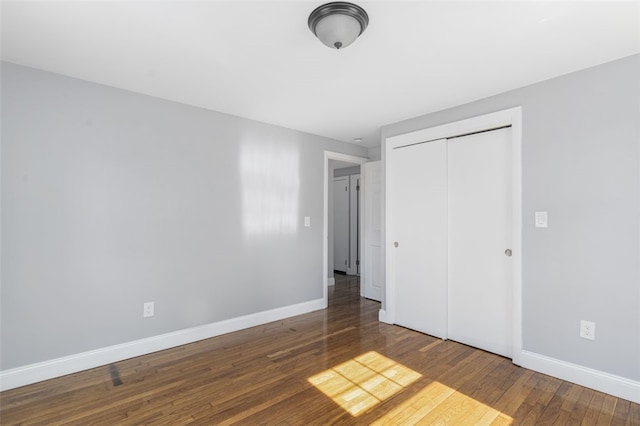 unfurnished bedroom with wood-type flooring, baseboards, and a closet