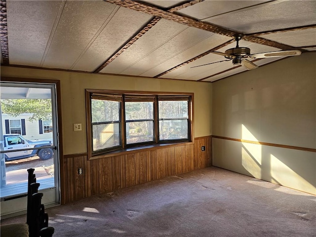 carpeted empty room featuring a wainscoted wall, ceiling fan, and wood walls