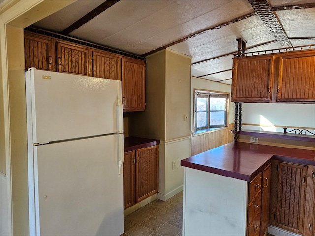 kitchen featuring freestanding refrigerator, brown cabinets, dark countertops, and dark tile patterned flooring