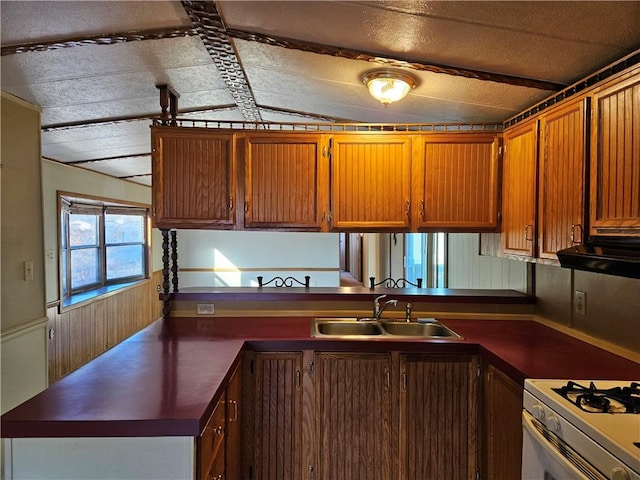 kitchen with a peninsula, brown cabinetry, dark countertops, and a sink