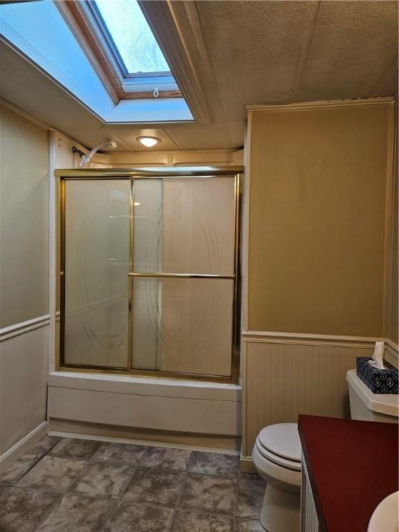 bathroom with toilet, bath / shower combo with glass door, a skylight, vanity, and wainscoting