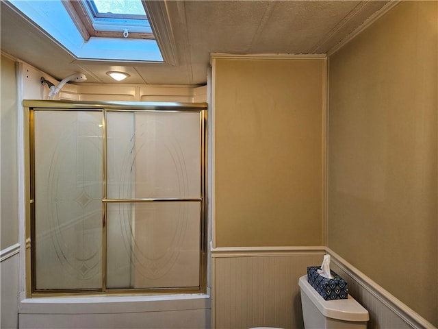 bathroom with toilet, a skylight, an enclosed shower, and a wainscoted wall