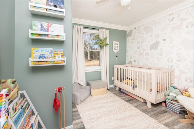 bedroom with wallpapered walls, baseboards, wood finished floors, crown molding, and a nursery area