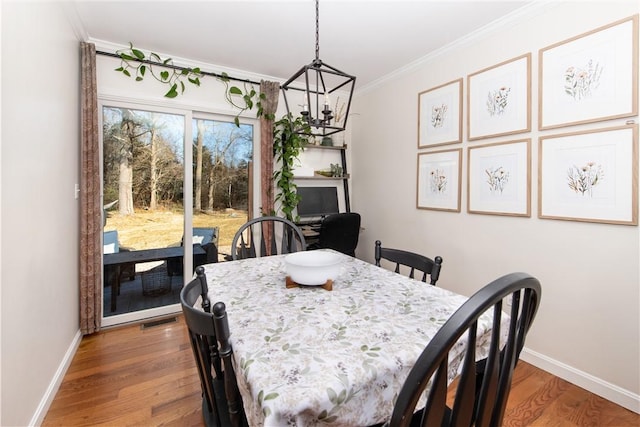 dining room featuring wood finished floors, visible vents, baseboards, ornamental molding, and an inviting chandelier