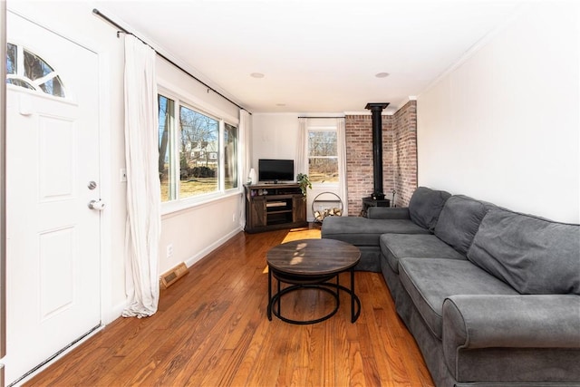 living room featuring visible vents, wood finished floors, a wood stove, and baseboards