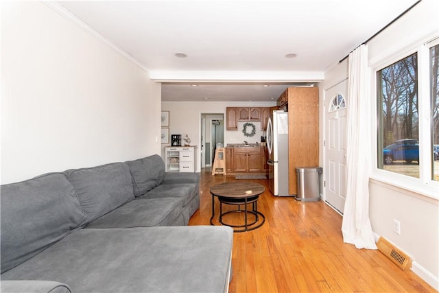 living area with visible vents, crown molding, light wood-style flooring, and baseboards