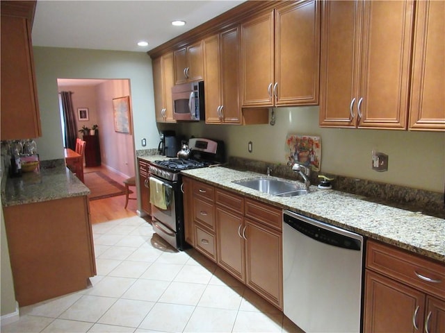 kitchen with brown cabinets, stainless steel appliances, recessed lighting, a sink, and light stone countertops