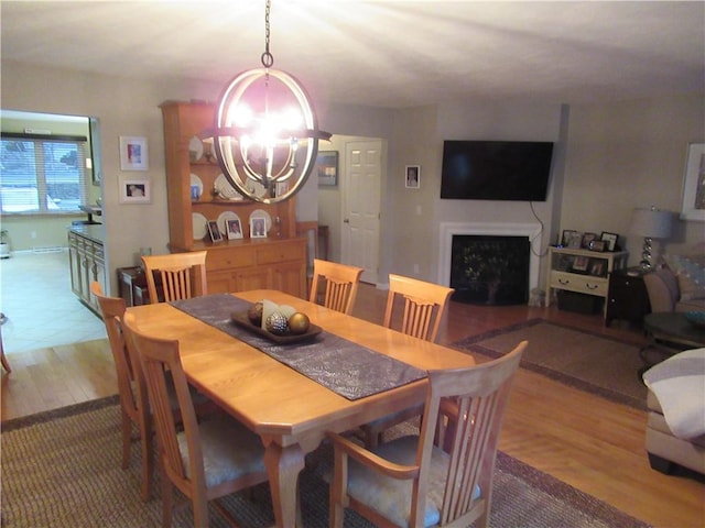 dining area with light wood-type flooring, a fireplace, and a notable chandelier