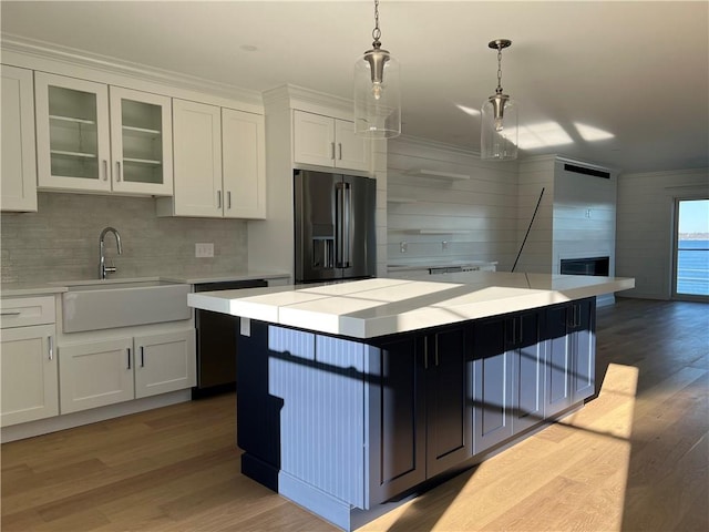 kitchen featuring light countertops, wood finished floors, black fridge with ice dispenser, white cabinets, and a sink