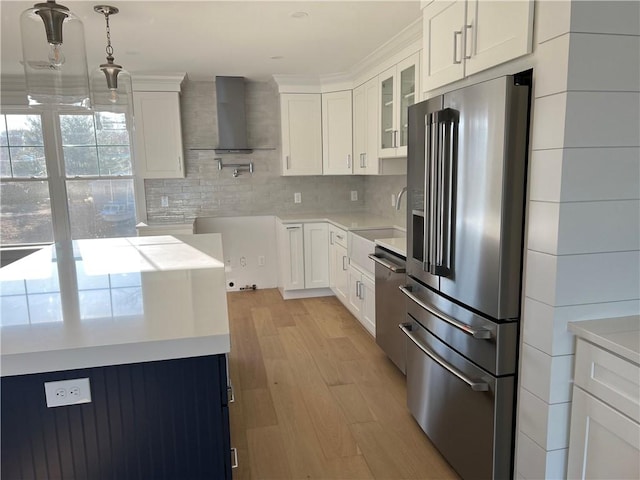 kitchen with a sink, glass insert cabinets, appliances with stainless steel finishes, wall chimney range hood, and light wood-type flooring