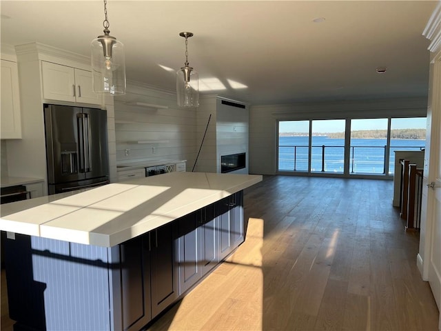 kitchen with wood finished floors, light countertops, white cabinets, a water view, and black fridge