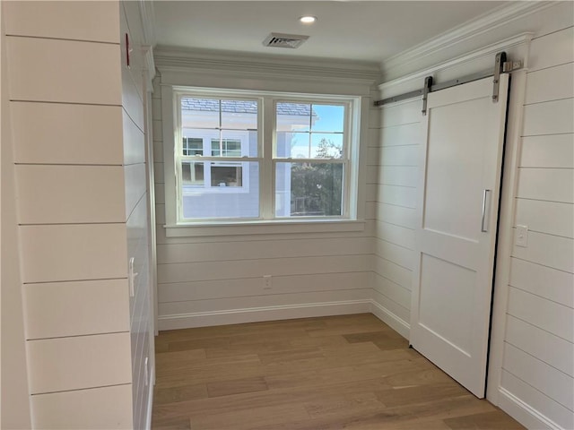 interior space featuring a barn door, visible vents, light wood-style flooring, and ornamental molding