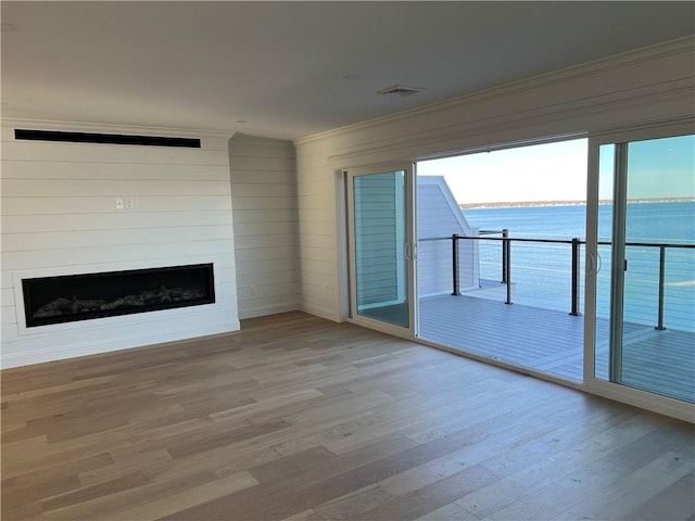 unfurnished living room with a healthy amount of sunlight, wood finished floors, a large fireplace, and a water view