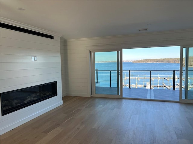 unfurnished living room with a wealth of natural light, wood finished floors, a large fireplace, and a water view