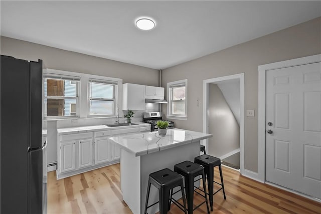 kitchen featuring stainless steel range with gas stovetop, a kitchen breakfast bar, freestanding refrigerator, under cabinet range hood, and a sink