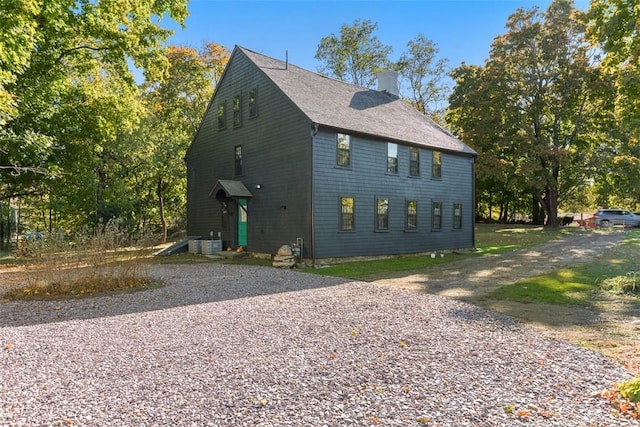 view of front of property featuring central air condition unit, driveway, a chimney, and roof with shingles