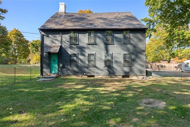 rear view of house featuring a chimney, a yard, and fence