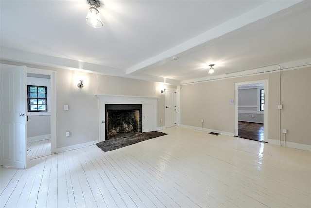 unfurnished living room with baseboards, visible vents, light wood finished floors, a fireplace with flush hearth, and beamed ceiling