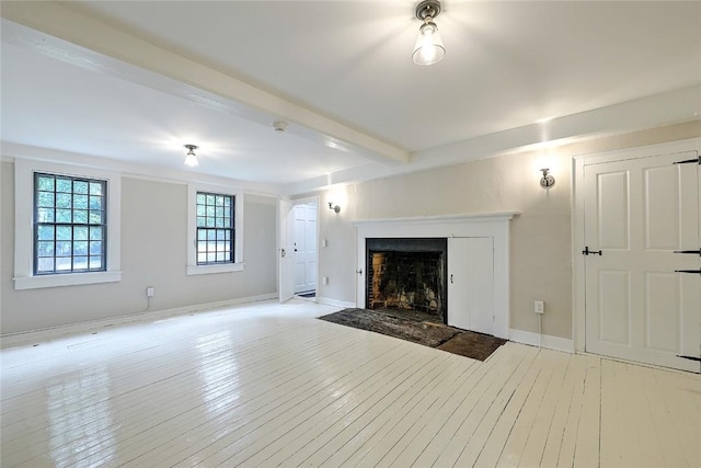 unfurnished living room featuring baseboards, beam ceiling, light wood-style flooring, and a fireplace with flush hearth