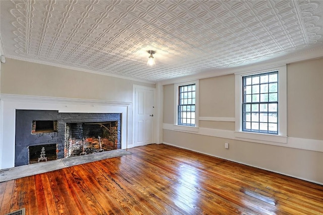 unfurnished living room with visible vents, an ornate ceiling, wood-type flooring, a fireplace, and crown molding