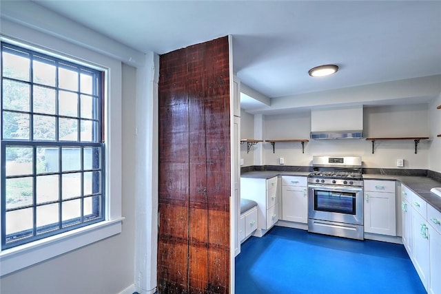 kitchen featuring open shelves, stainless steel range with gas cooktop, dark countertops, and a wealth of natural light