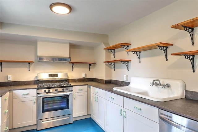 kitchen featuring open shelves, a sink, dark countertops, stainless steel appliances, and wall chimney range hood