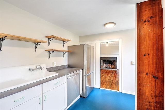 kitchen with open shelves, a fireplace, a sink, appliances with stainless steel finishes, and white cabinetry