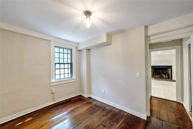 spare room featuring a fireplace, dark wood-type flooring, and baseboards