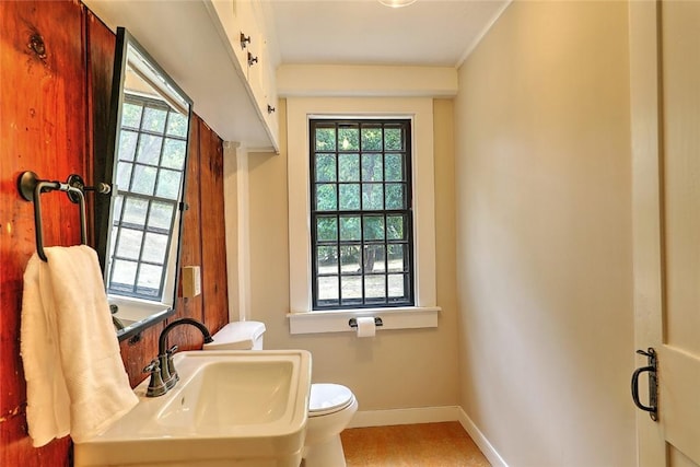 half bath featuring a healthy amount of sunlight, baseboards, and a sink