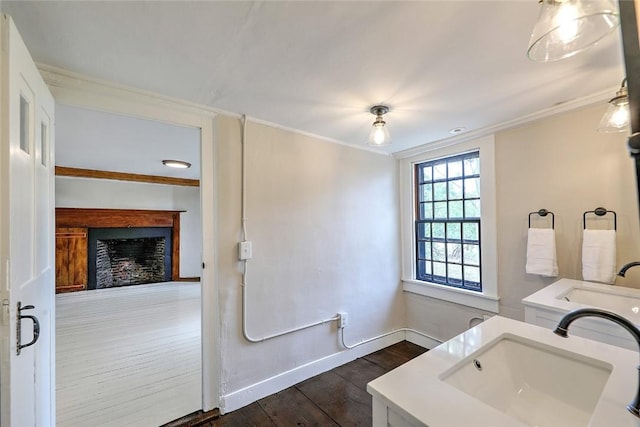 bathroom featuring vanity, wood finished floors, baseboards, a fireplace, and crown molding