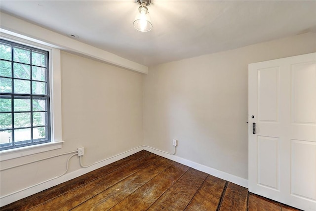 spare room with baseboards and dark wood-style floors