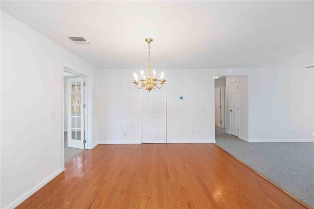 spare room with baseboards, visible vents, a notable chandelier, and light wood finished floors