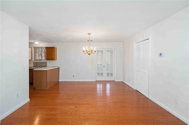 unfurnished dining area with light wood finished floors, a notable chandelier, baseboards, and a sink