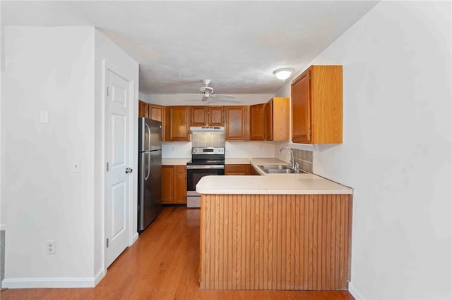 kitchen featuring stainless steel appliances, light countertops, a sink, a peninsula, and under cabinet range hood