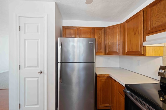 kitchen featuring brown cabinetry, stainless steel appliances, light countertops, a textured ceiling, and under cabinet range hood