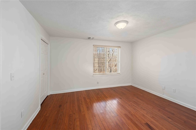 spare room with a textured ceiling, hardwood / wood-style floors, visible vents, and baseboards