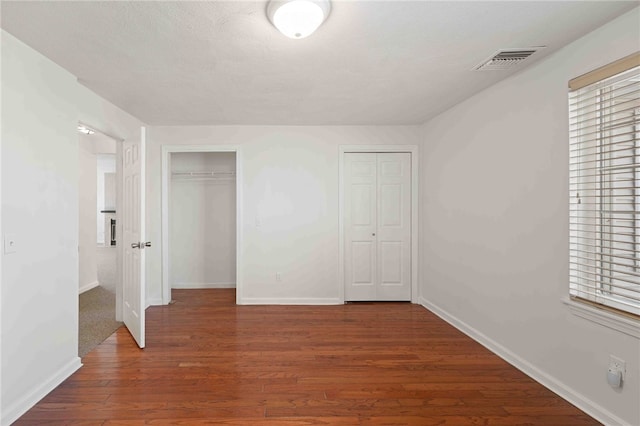 unfurnished bedroom with baseboards, visible vents, multiple closets, and wood finished floors