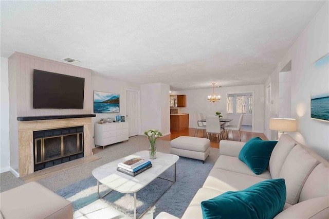 carpeted living room with a textured ceiling, a premium fireplace, visible vents, and a notable chandelier