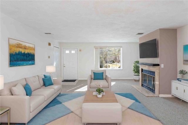 carpeted living area with a textured ceiling, a high end fireplace, visible vents, and baseboards