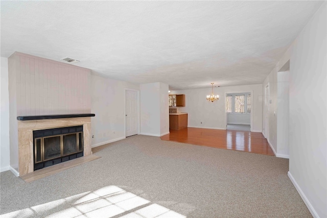 unfurnished living room featuring a fireplace with raised hearth, a chandelier, visible vents, baseboards, and carpet