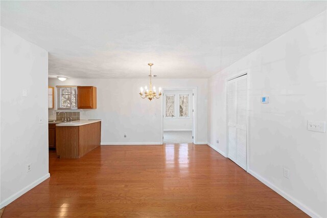 unfurnished dining area with a sink, baseboards, a chandelier, and wood finished floors