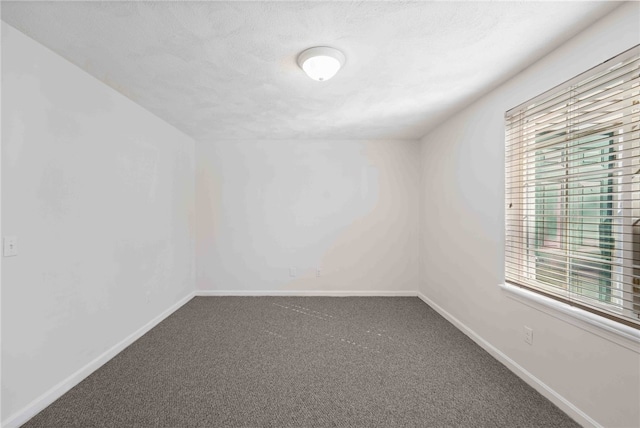 spare room with a textured ceiling, carpet, and baseboards