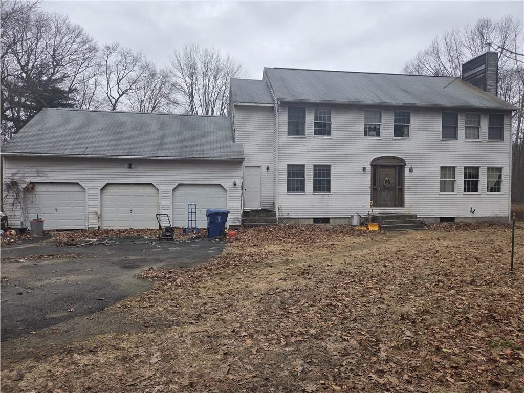 colonial house featuring entry steps, driveway, a chimney, metal roof, and an attached garage