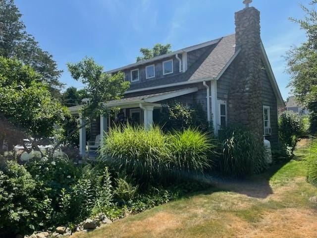 view of side of property with a shingled roof, a chimney, and a lawn