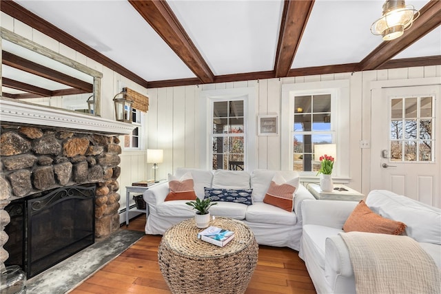 living room featuring a baseboard radiator, beamed ceiling, hardwood / wood-style floors, and a stone fireplace