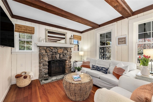 living room with hardwood / wood-style flooring, beamed ceiling, and a stone fireplace