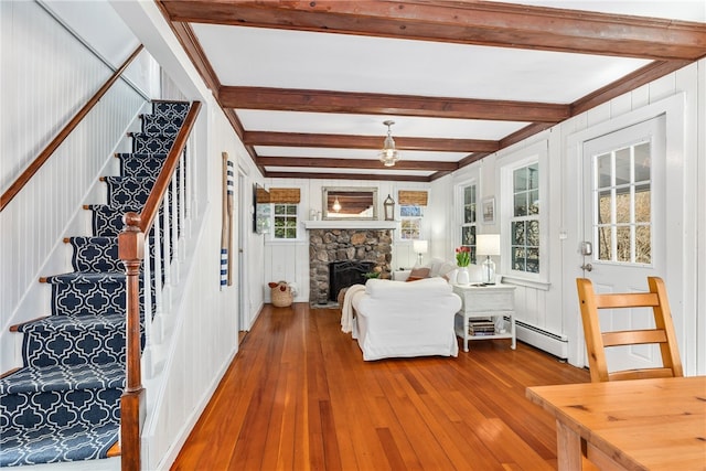 unfurnished living room with wood-type flooring, stairway, a fireplace, a baseboard heating unit, and beam ceiling