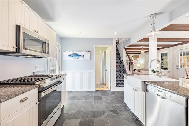 kitchen featuring a wainscoted wall, decorative light fixtures, stainless steel appliances, a sink, and beamed ceiling