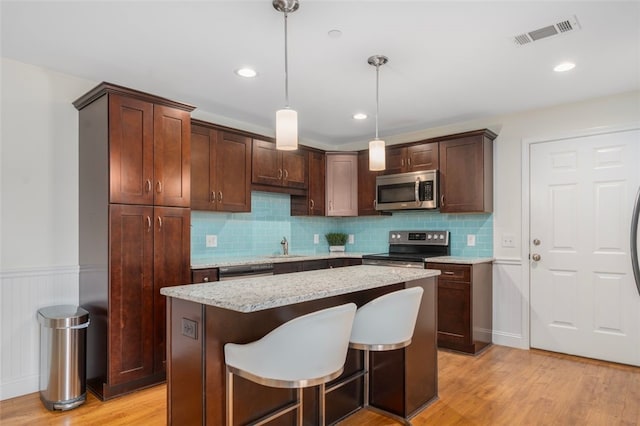 kitchen featuring visible vents, a kitchen island, stainless steel appliances, light wood-type flooring, and pendant lighting