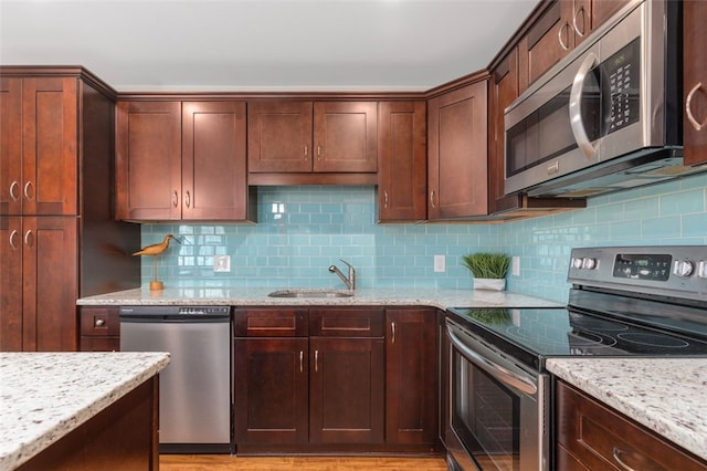 kitchen featuring stainless steel appliances, light stone counters, a sink, and decorative backsplash